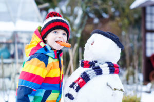 36716845 - funny little kid boy making a snowman and eating carrot, playing and having fun with snow, outdoors on cold day. active outoors leisure with children in winter.