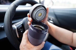 Asian woman driver hold thermo mug with hot coffee in car, danger