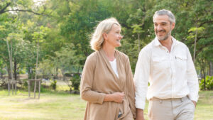 Smiling senior man and woman holding hand and walking at park, Love marriage life goals, Happy retirement elder couple spending time, talking, sharing and relaxing together concept, banner size