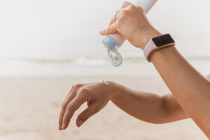 Woman squeezes sunscreen out of a tube on the sea beach UV protection