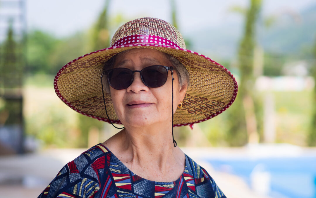 Portrait of senior woman wearing sunglasses and straw hat while standing side swimming pool. Space for text. Concept of aged people and relaxation.