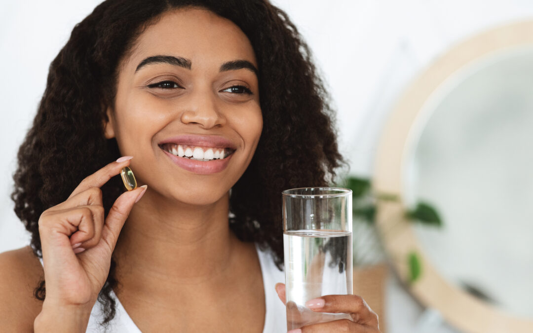 Daily Intake Of Vitamins And Minerals. Happy Black Woman Holding Capsule With Beauty Supplements And Water Glass, Closeup