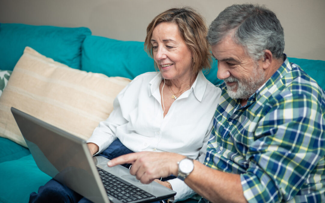 Elderly retired couple pointing at computer screen while discovering new technologies from the sofa at home